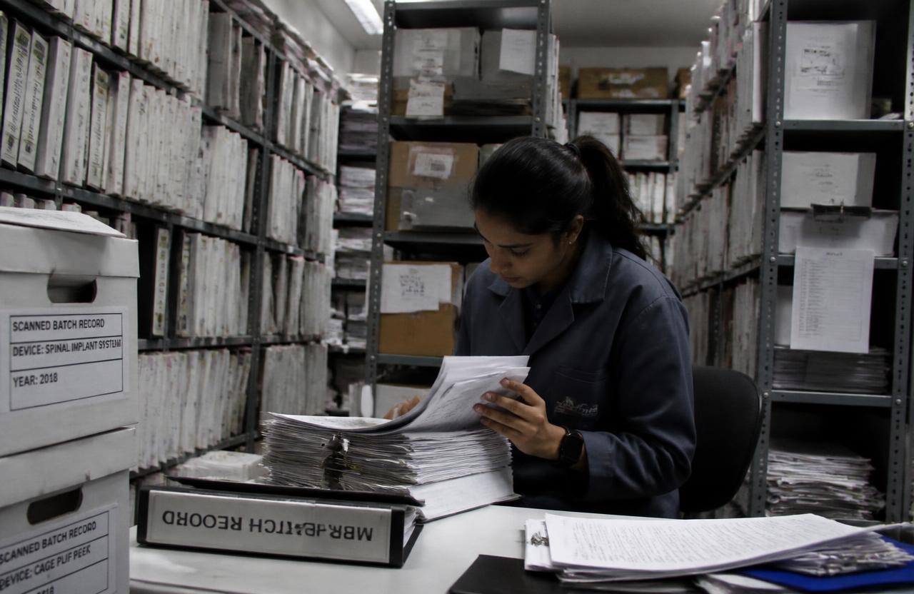 Analista de calidad buscando entre carpetas de registros de lote en un cuarto de archivo